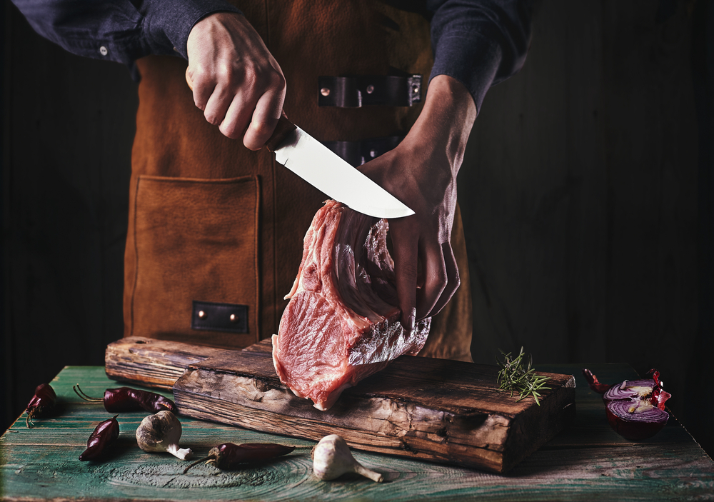 A,guy,in,a,leather,apron,is,slicing,raw,meat.